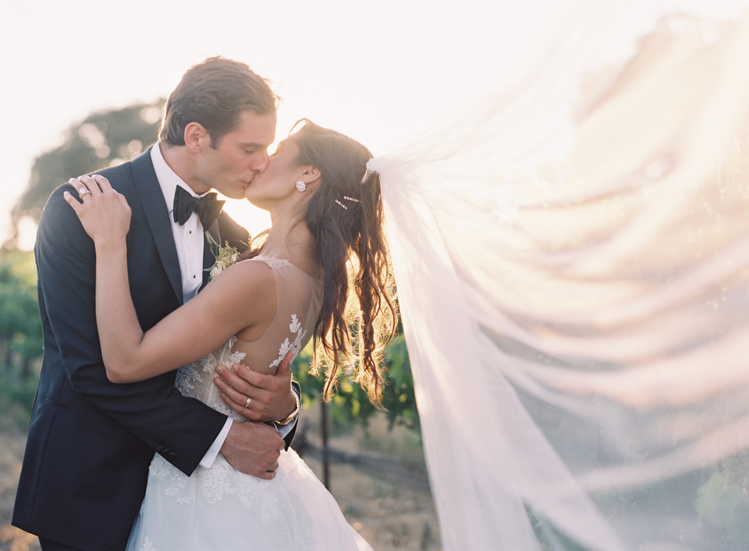 Newlyweds kissing at sunset with veil catching in the wind