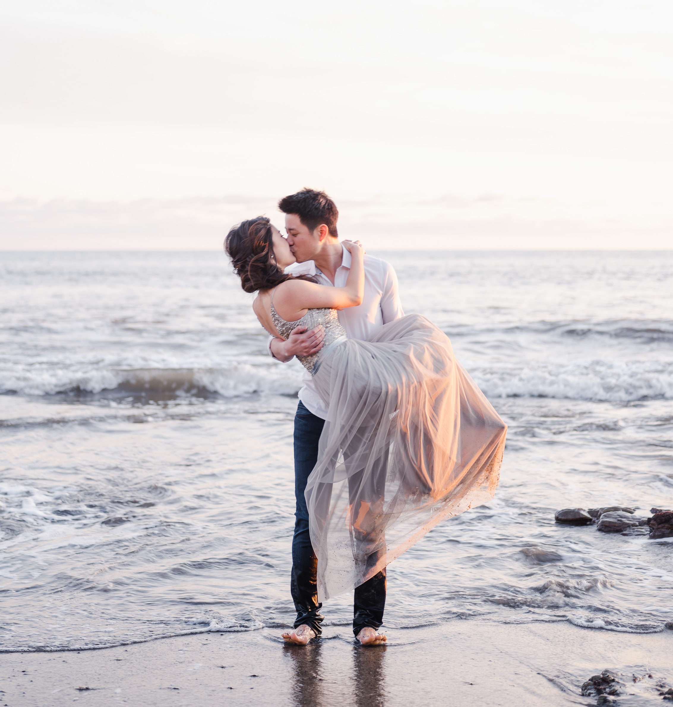 Man holding woman in his arms kissing on the beach in the waves