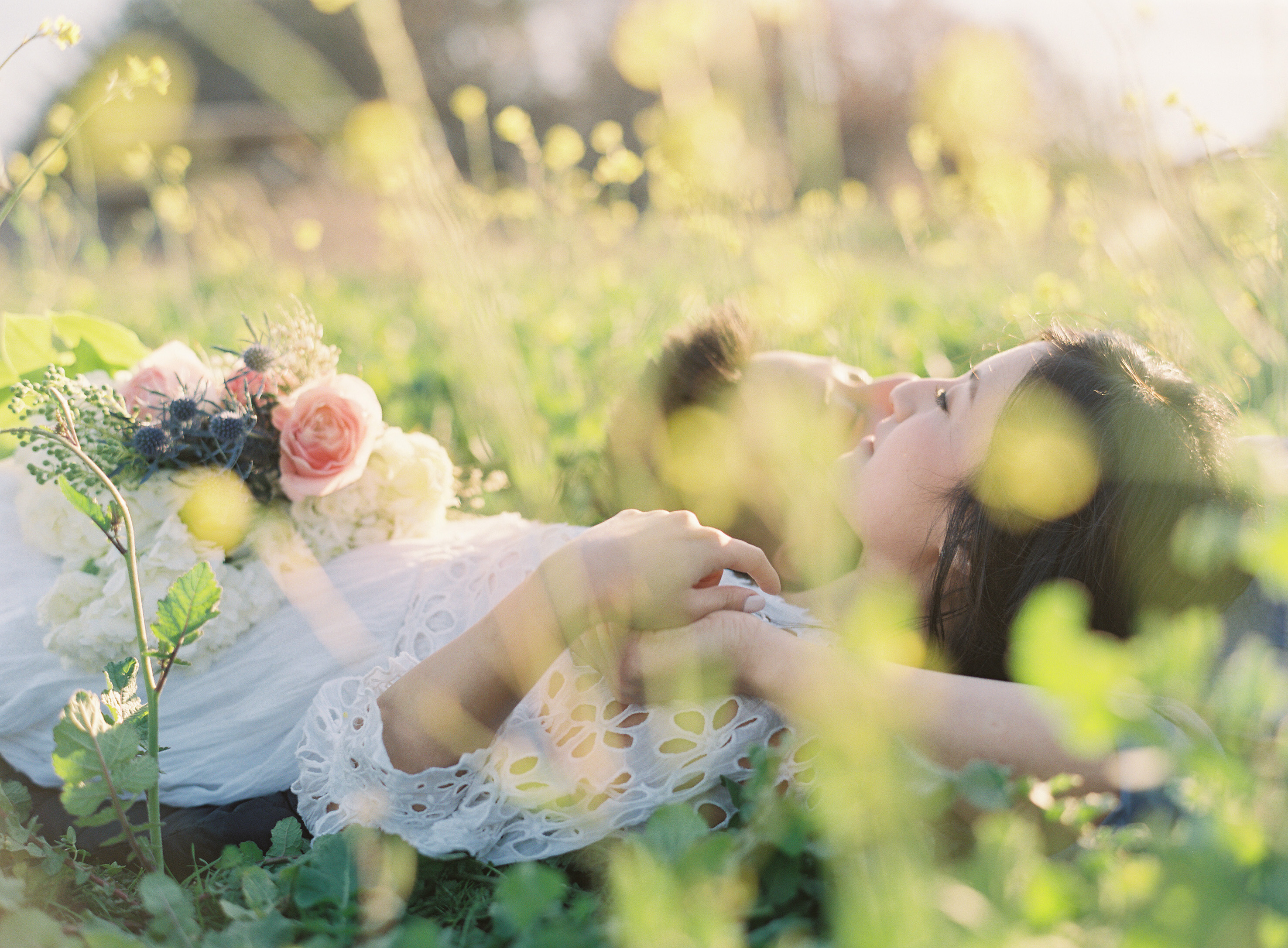 Couple laying on grass together with yellow flowers blurry in front of them