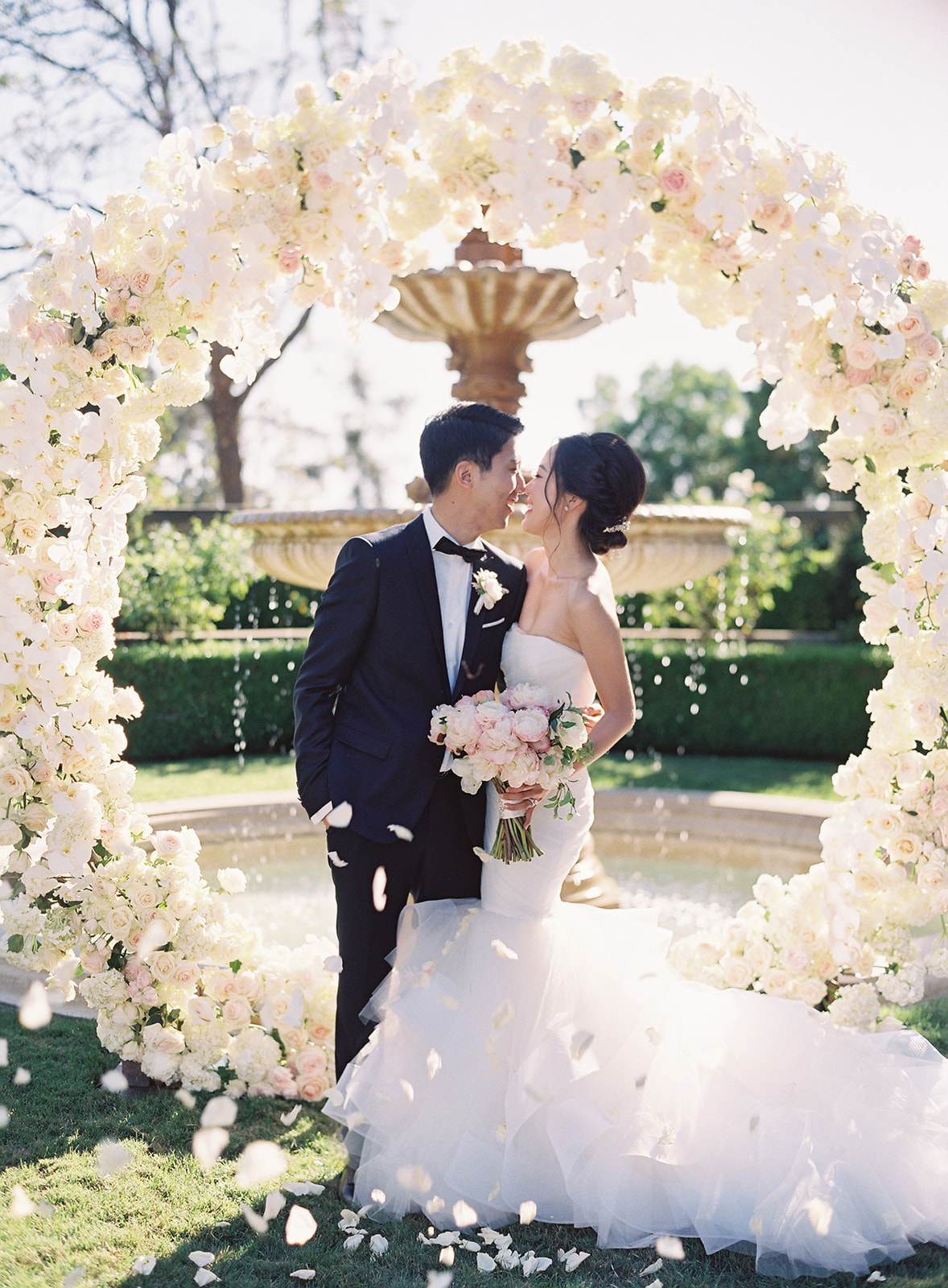 Couple under a life size floral arch holding each other and laughing