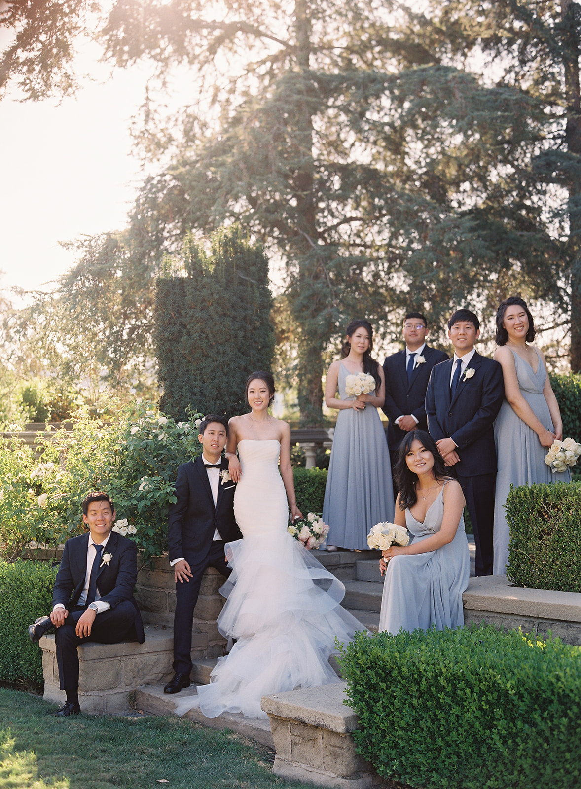 Photo of bridal party surrounding bride and groom and coupled together on stairs and positioned in different heights