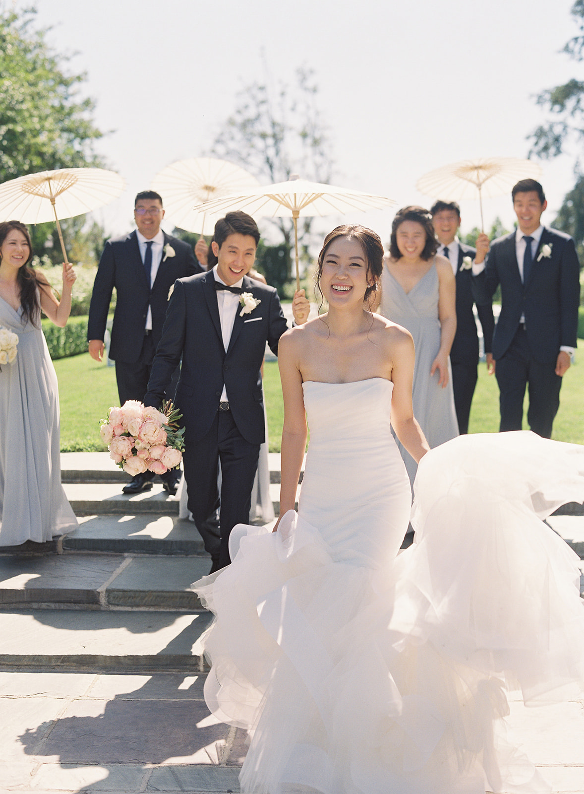 Bridal party holding paper umbrellas walking after bride