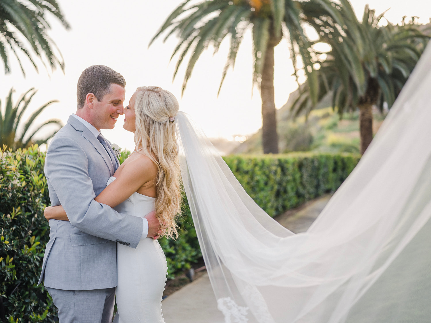 bride and groom holding each other and looking into each others eyes as brides veil floats in the air