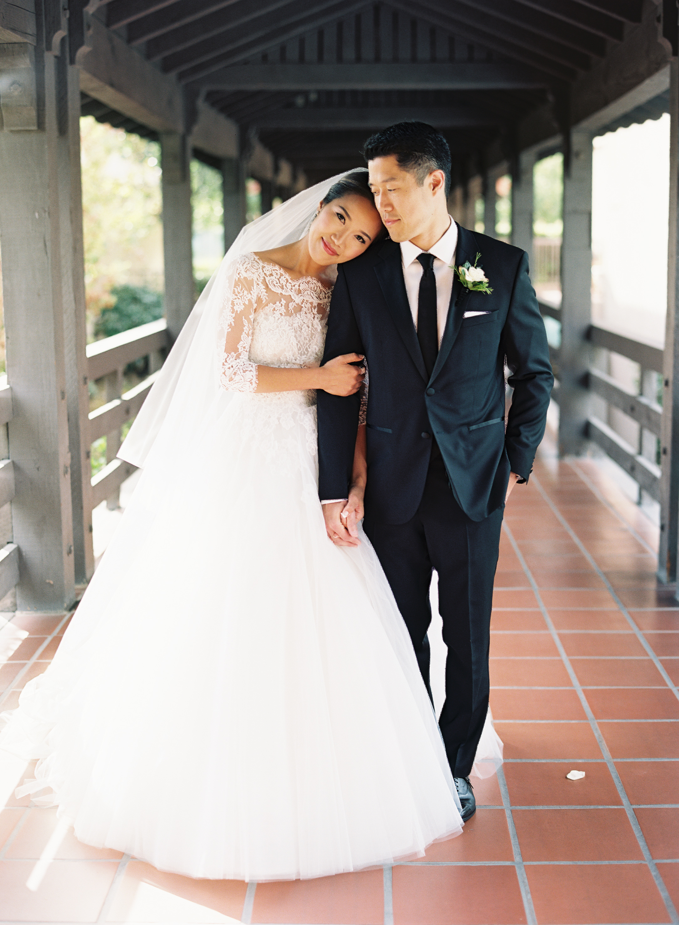 Bride and groom on a bridge holding hands, brides head resting on grooms shoulder