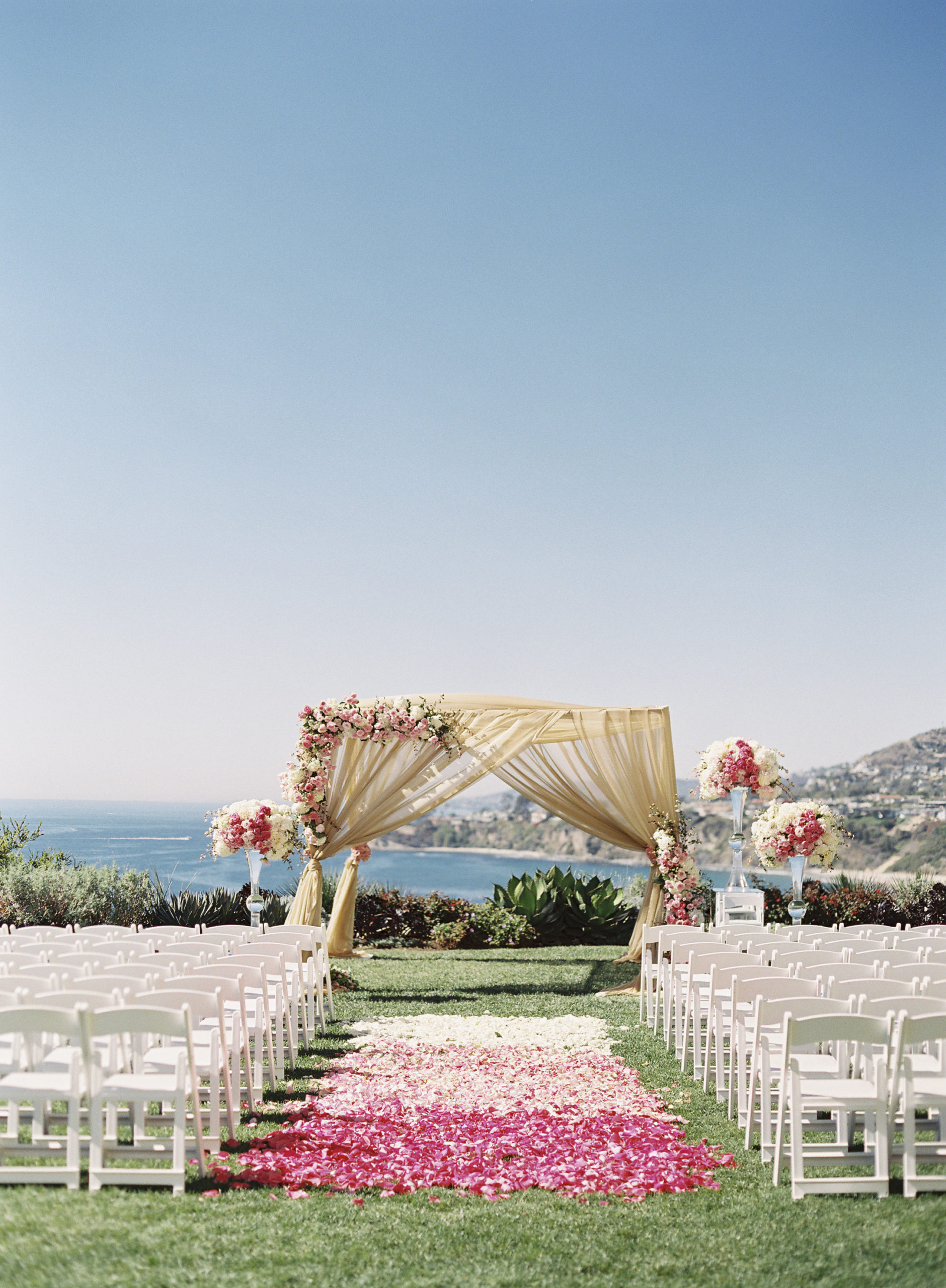 Wedding alter overlooking the ocean with white and pink flower pedals down the aisle