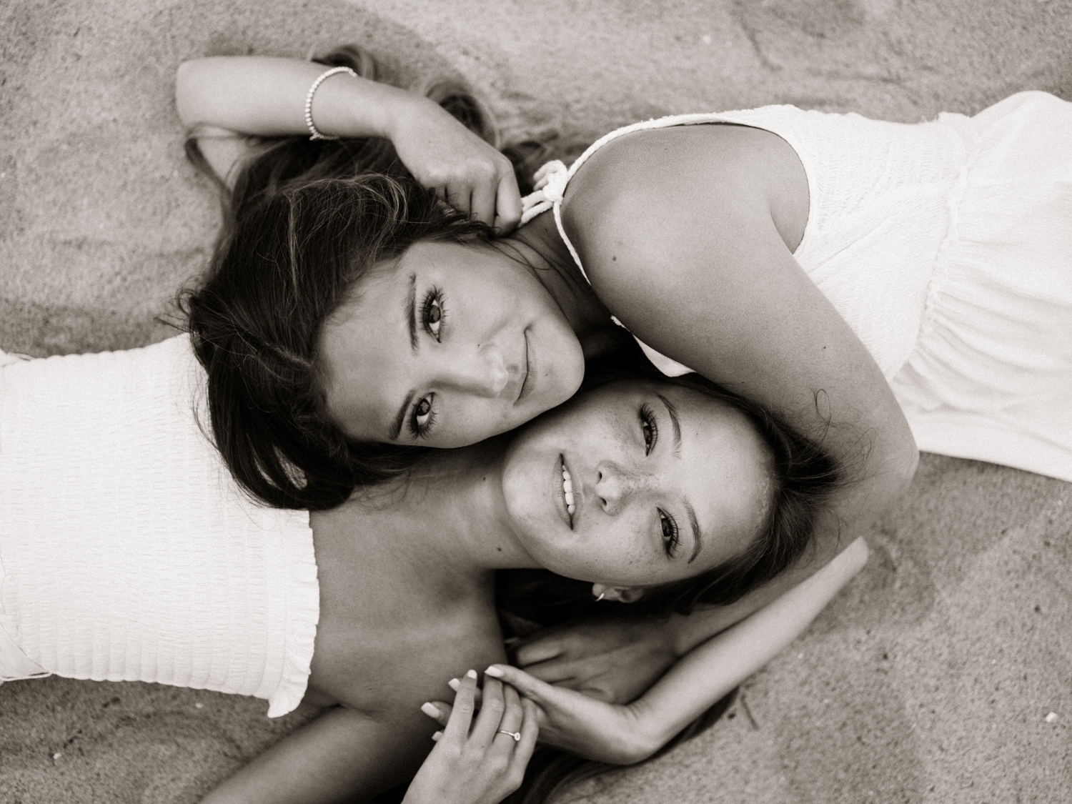 Two sisters look up at the camera lying down on the sand