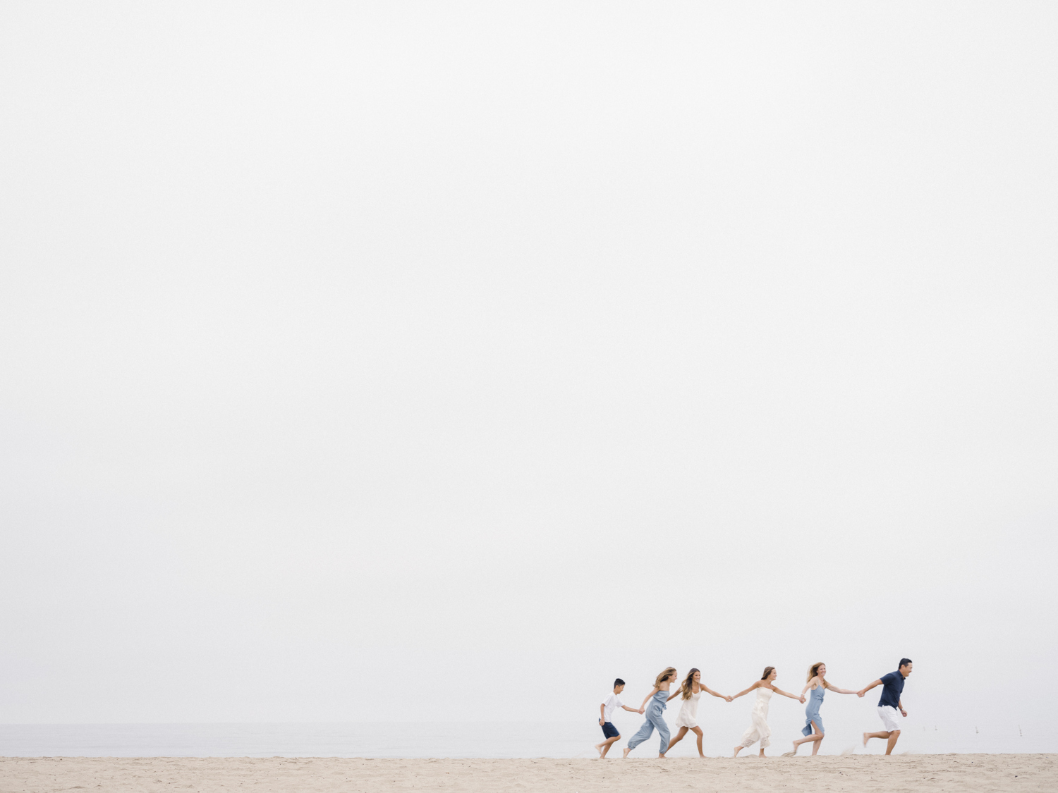 Photo of family holding hands in a single file line running on the beach together