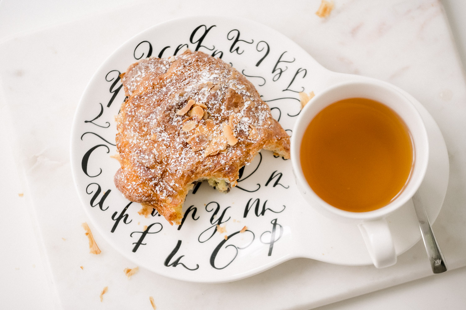 Overhead photo of plate and saucer with tea and crouissant
