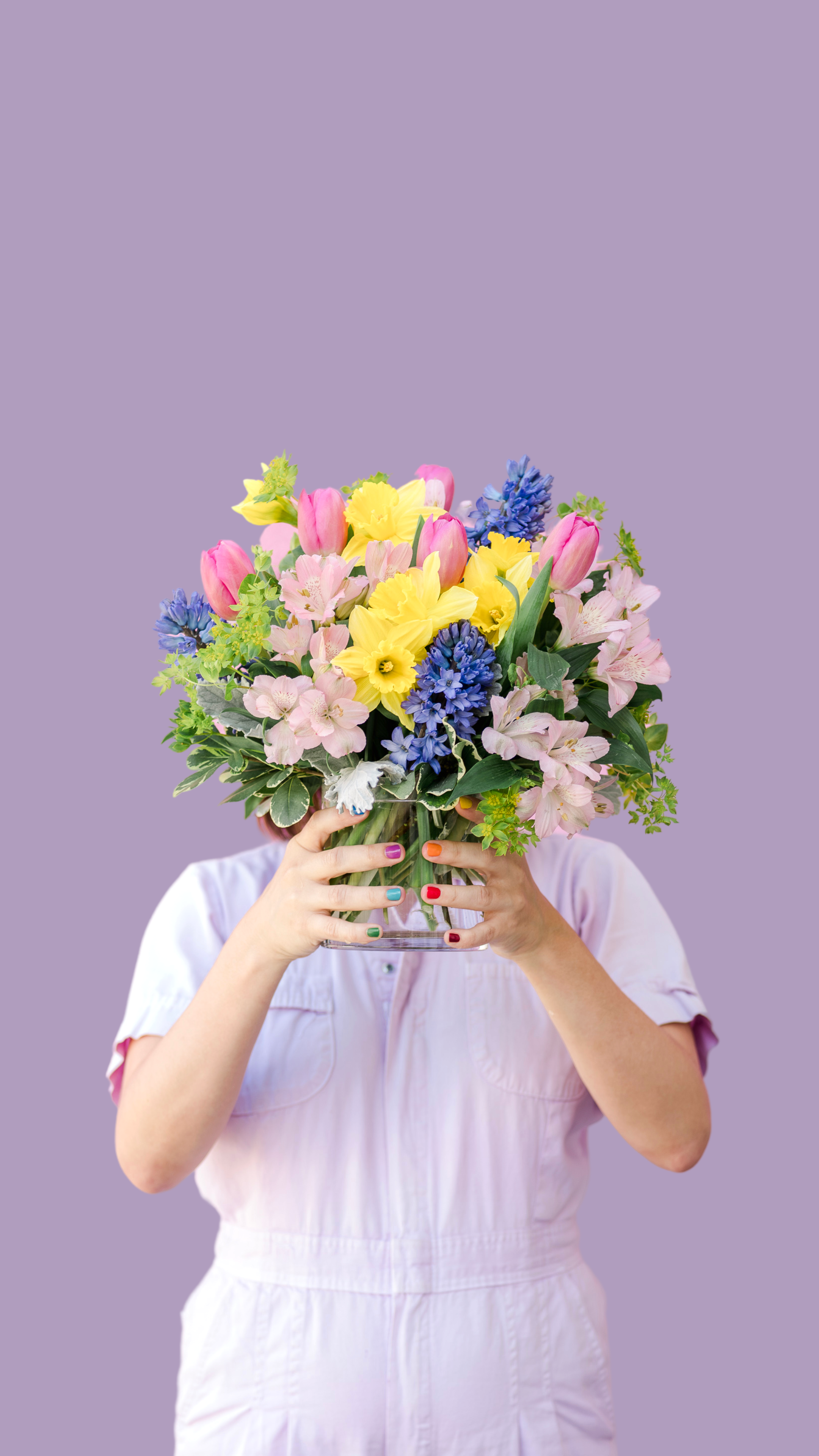 girl in a lavender jumpsuit holding a bouquet of spring florals in front of her face
